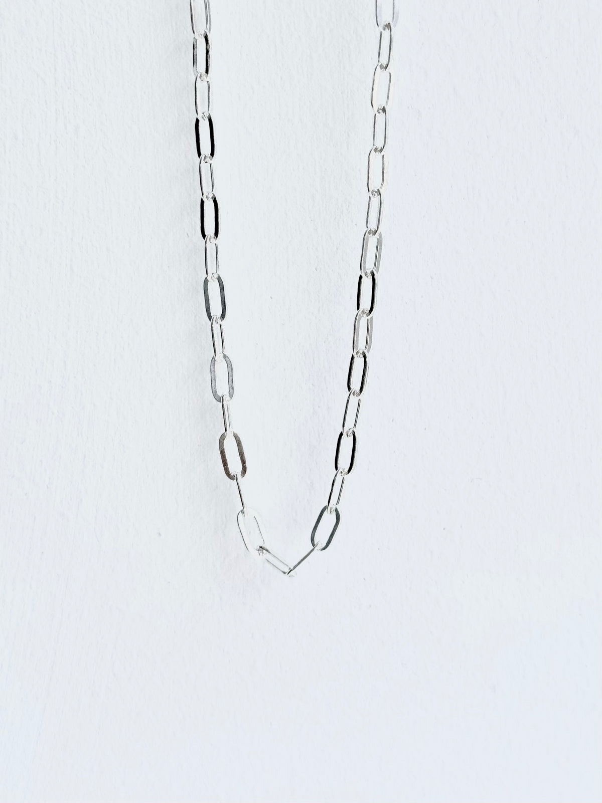 Silver chain necklace on a light gray background paperclip style small guage