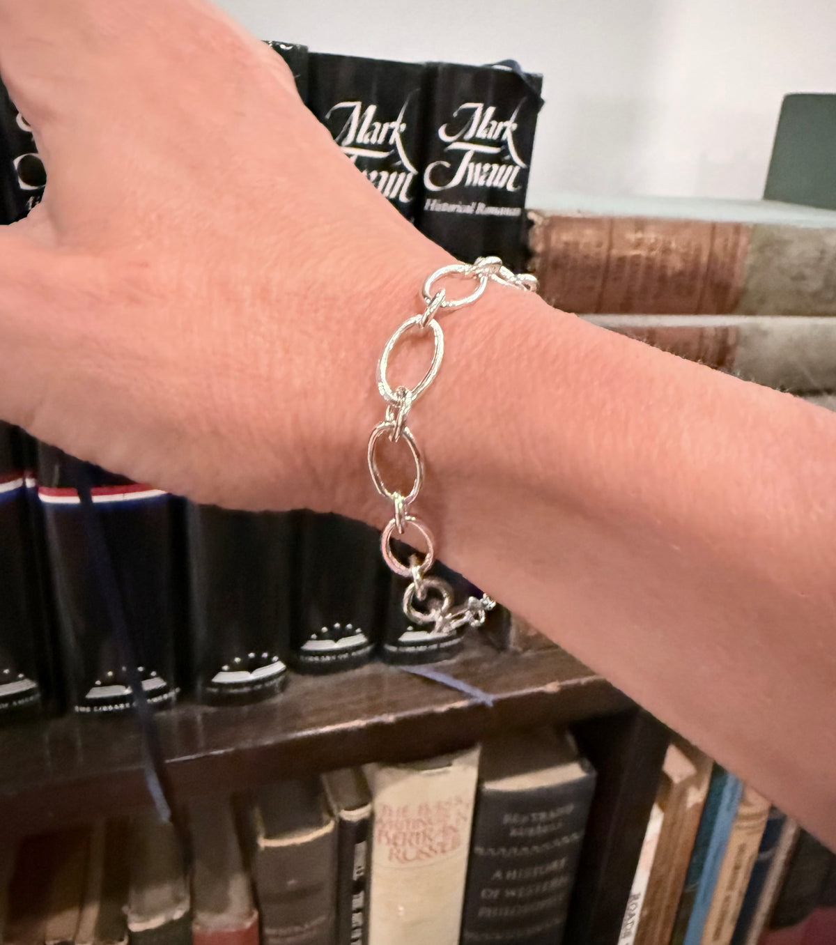 closeup of silver bracelet with books in the background