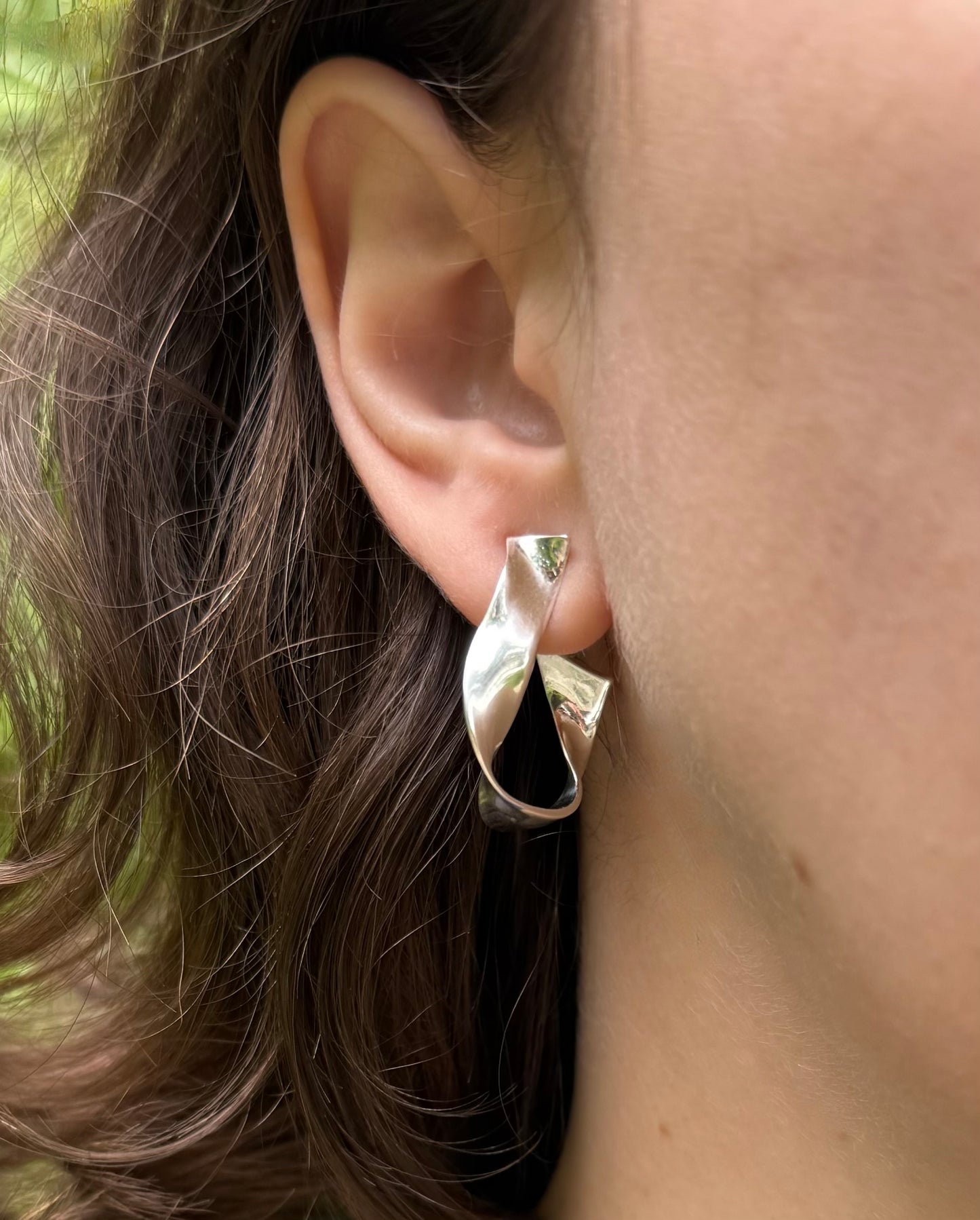 Silver earring worn by a person with brown hair.