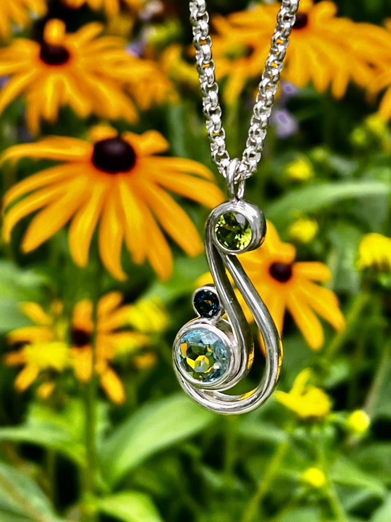 aria pendant by hannah daye & co in peridot and london blue topaz and sky blue topaz shown with black eyed susans