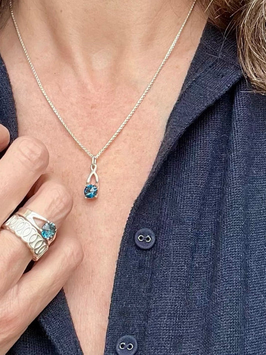 wearing London Blue Topaz Brillante Charm pendant with Brillante Ring and Oslo Band Ring all by Hannah Daye & Co jewelry design