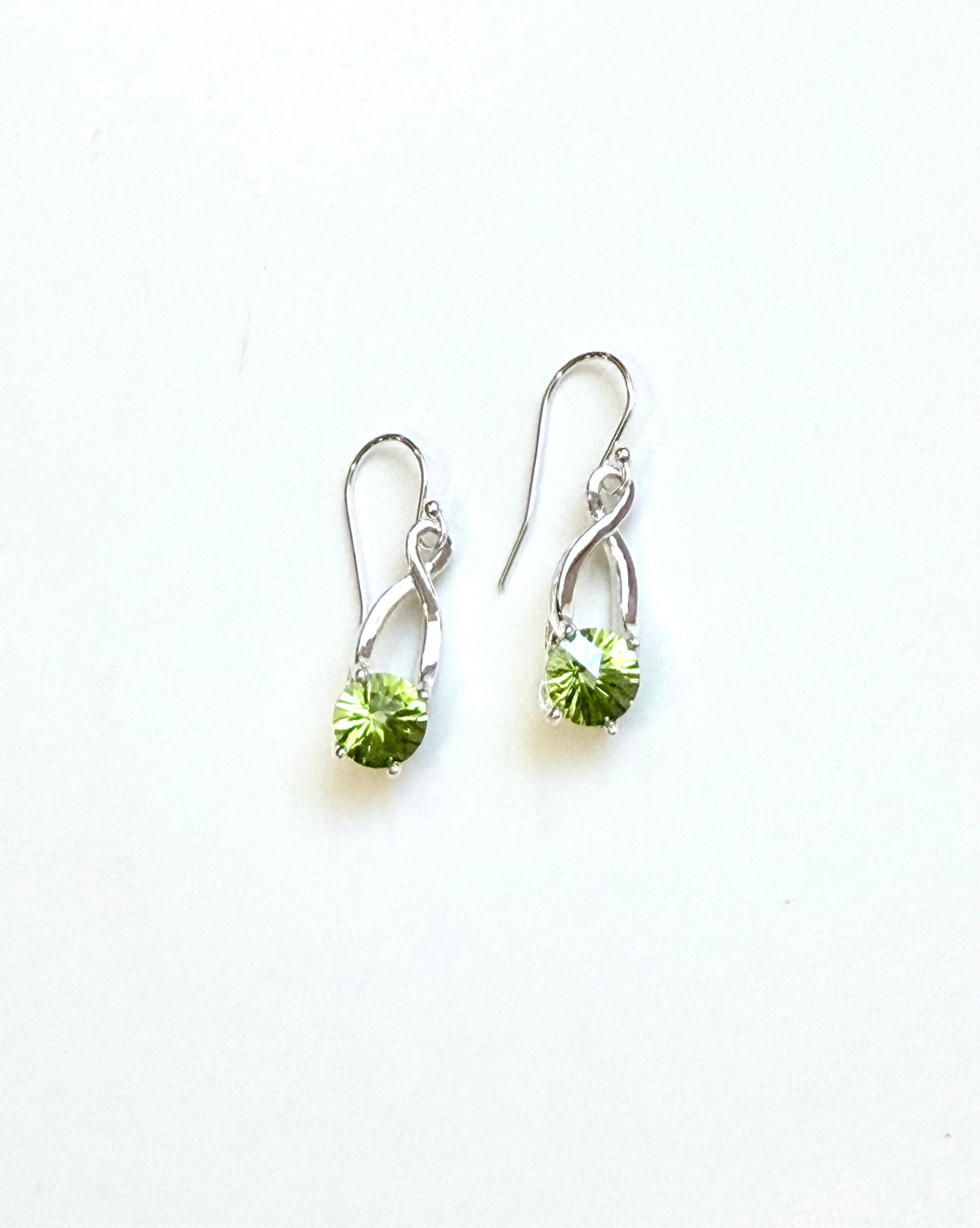 A pair of silver drop earrings with bright green faceted gemstones shown on a plain white background.