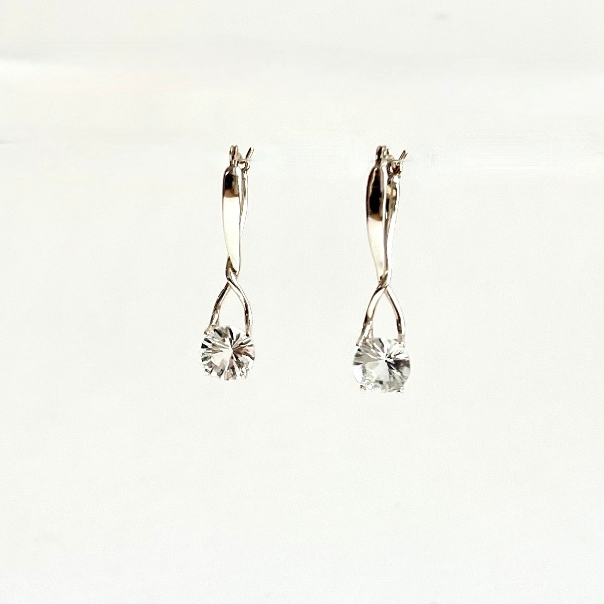 A pair of silver earrings with clear faceted round gemstones, displayed against a plain white background.