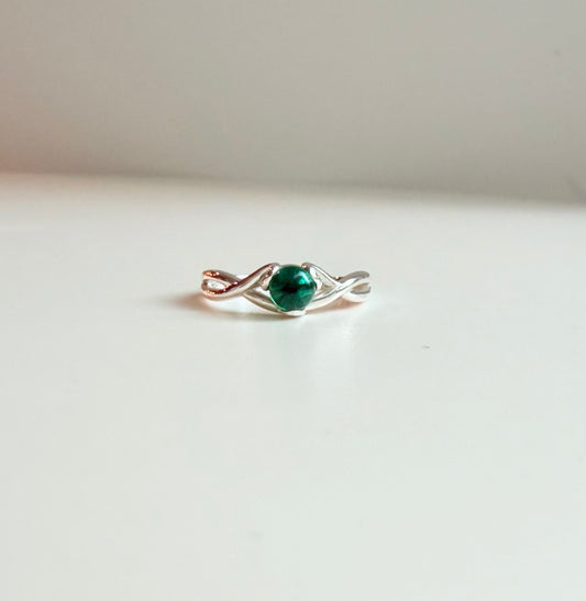 A delicate ring with a silver-toned twisted band, a central round green gemstone, photographed on a plain white surface.