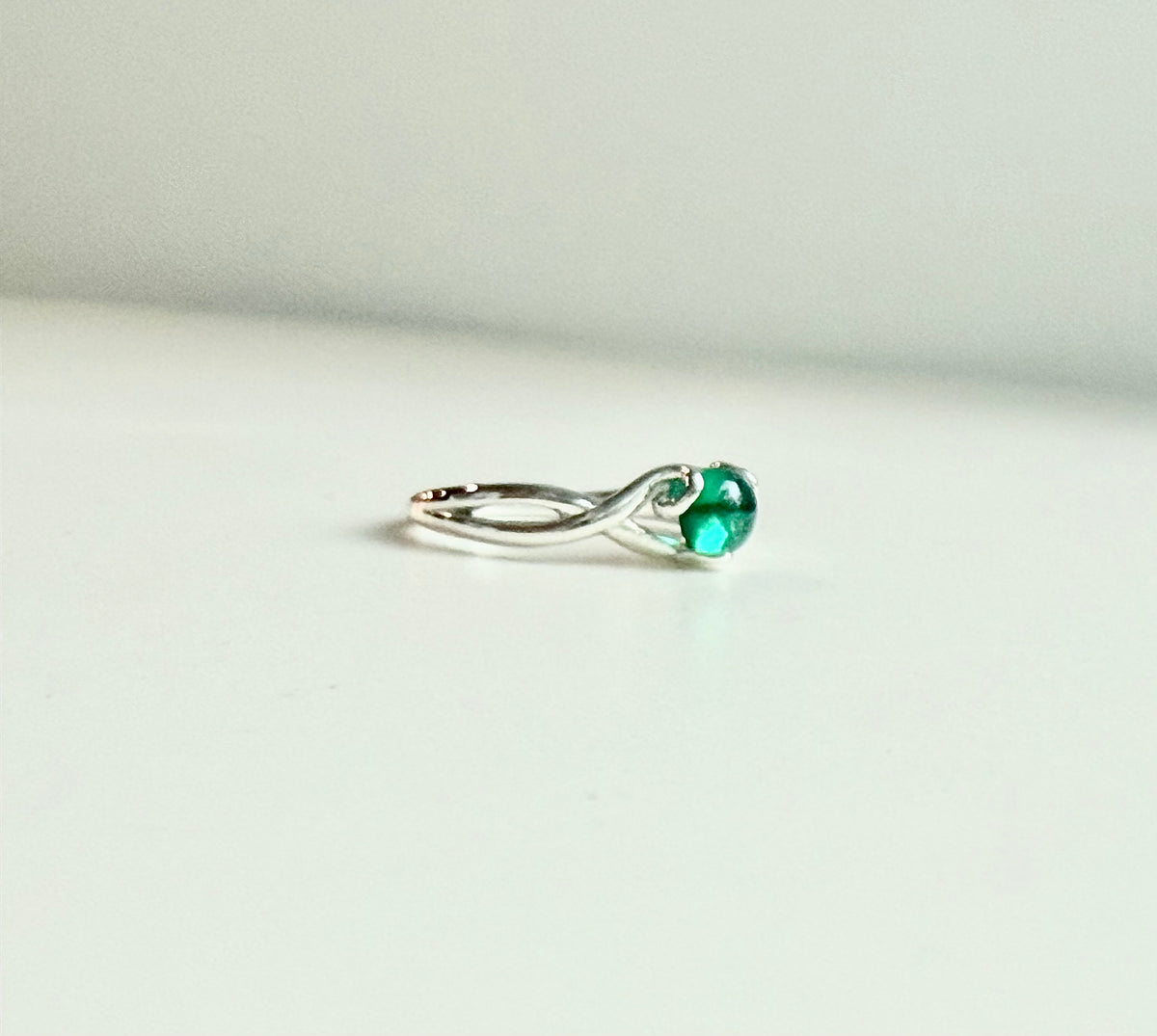 A silver ring with a twisted band and a round green gemstone, photographed on a plain light background.