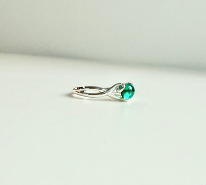 A silver ring with a twisted band and a round green gemstone, photographed on a plain light background.