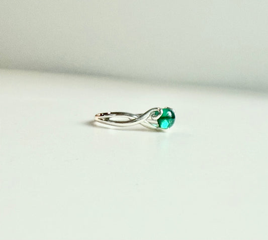 A silver ring with a twisted band and a round green gemstone, photographed on a plain light background.