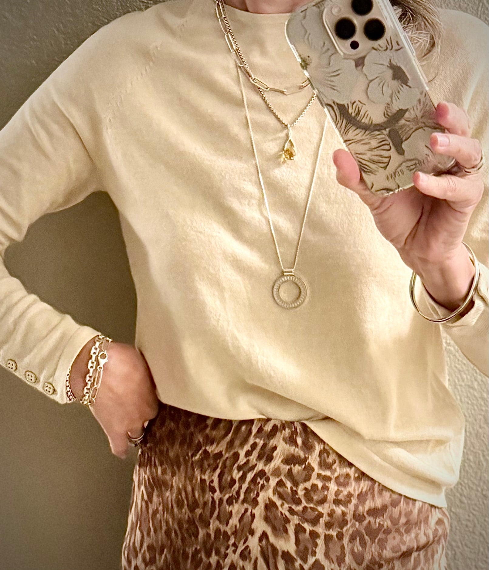 Person wearing a beige long-sleeve top and leopard print skirt, and silver jewelry necklaces and bracelets
