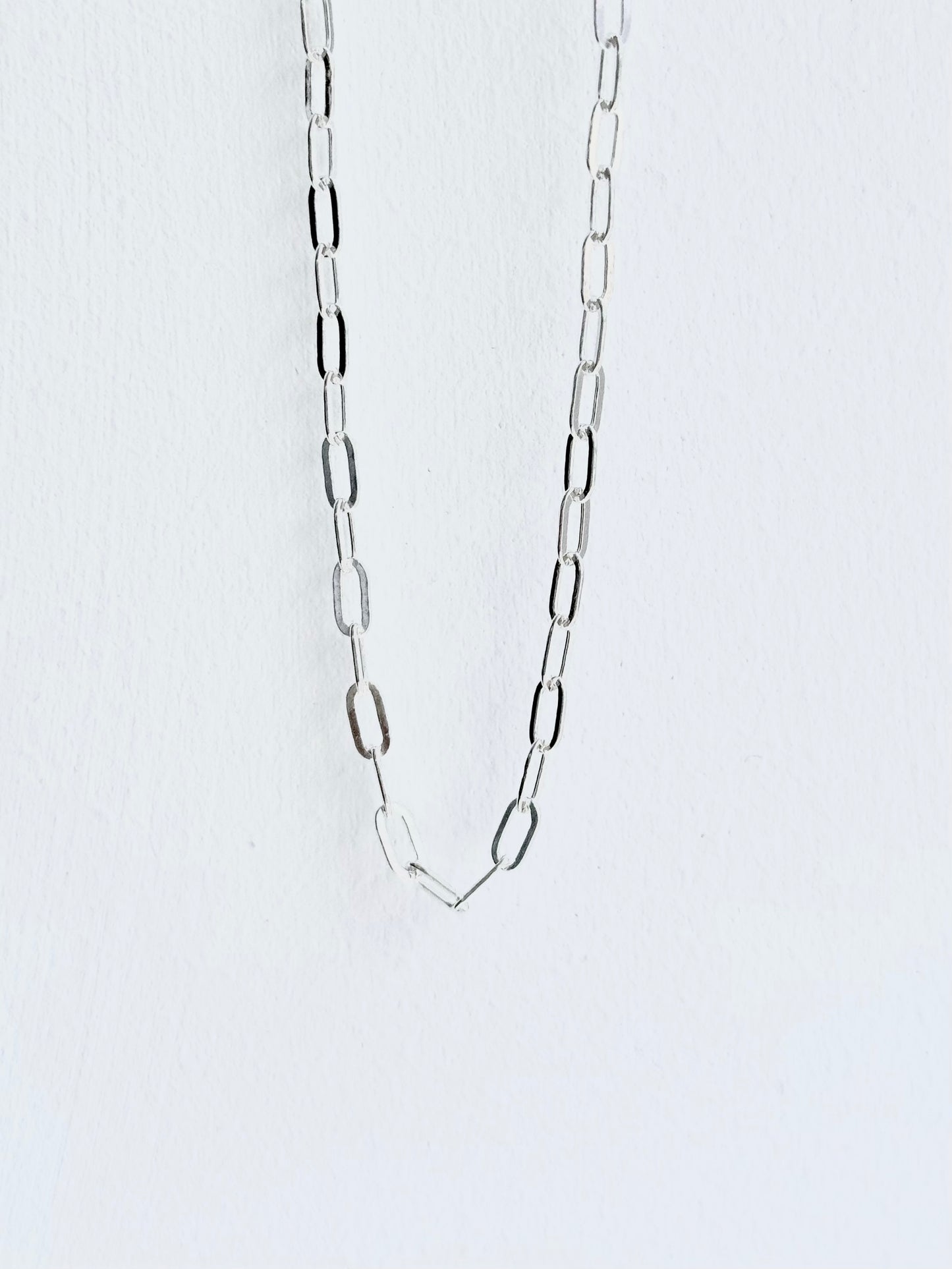 Silver chain necklace on a light gray background paperclip style small guage