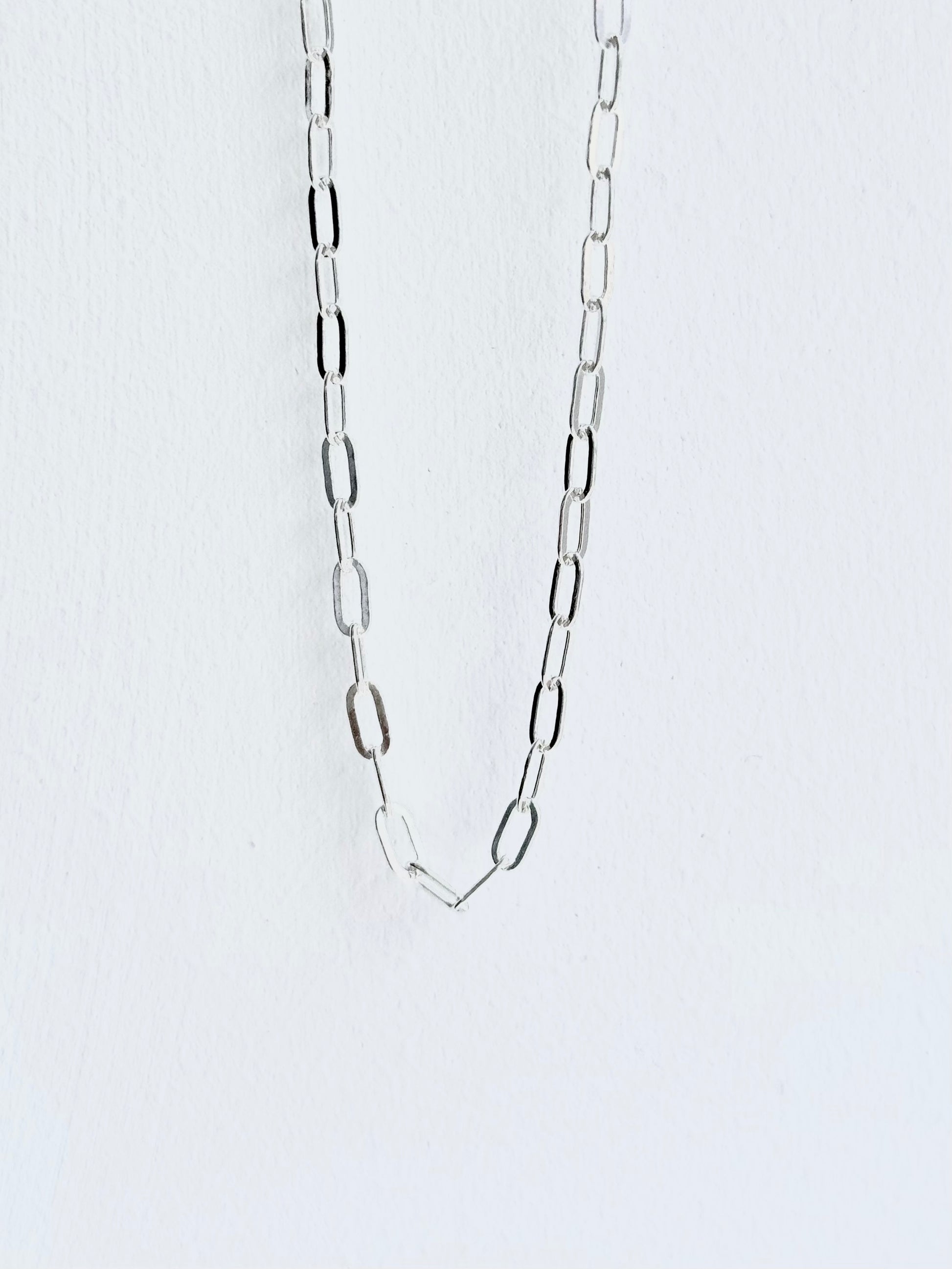 Silver chain necklace on a light gray background paperclip style small guage