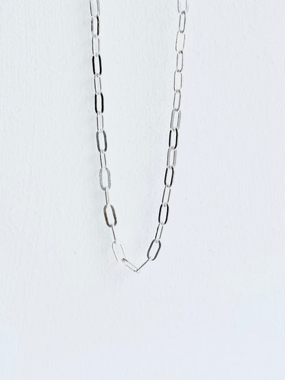 Silver chain necklace on a light gray background paperclip style small guage