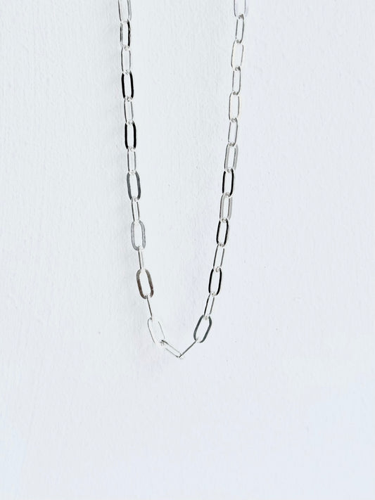 Silver chain necklace on a light gray background paperclip style small guage