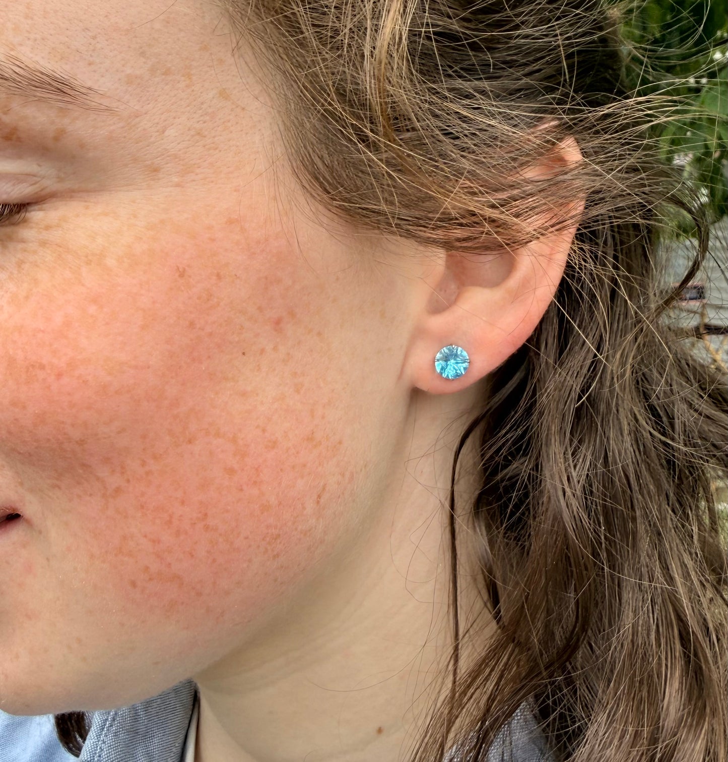 Close-up of a person wearing a blue gemstone earring outdoors.
