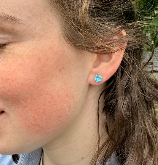 Close-up of a person wearing a blue gemstone earring outdoors.