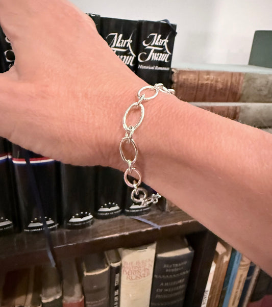 closeup of silver bracelet with books in the background