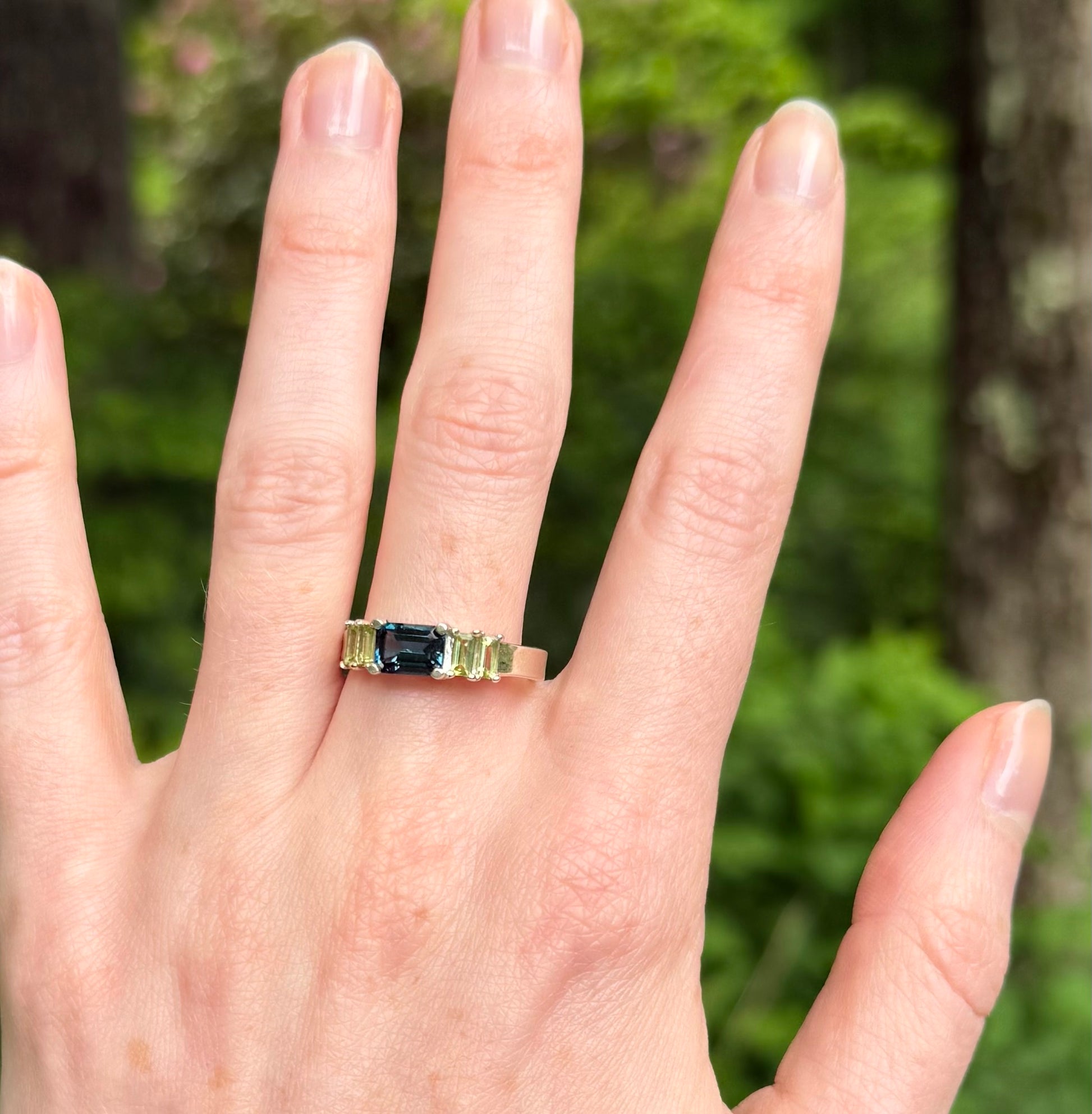 Ring with a blue and green gemstones on a hand against a blurred green background