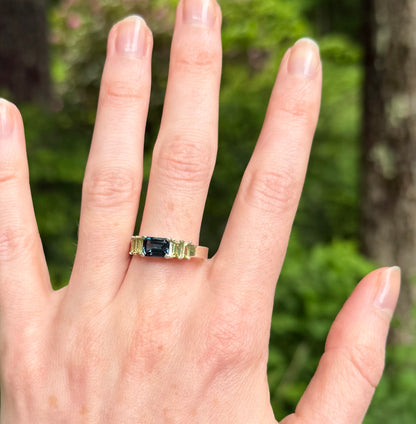 Ring with a blue and green gemstones on a hand against a blurred green background