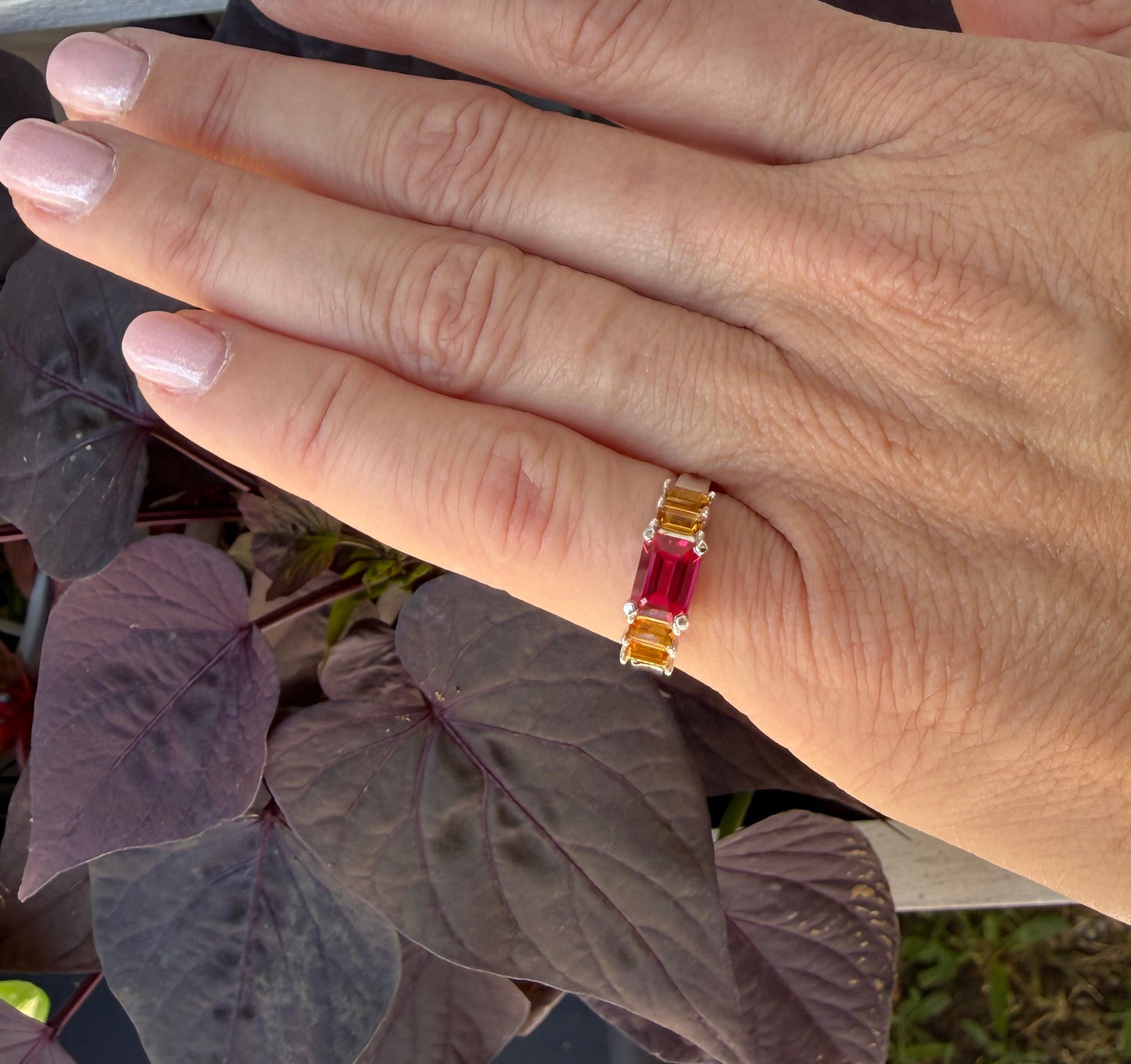 Hand wearing a ring with a red gemstone outdoors