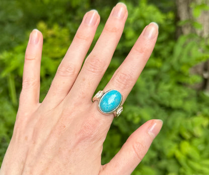 Hand wearing a turquoise ring with a green leafy background