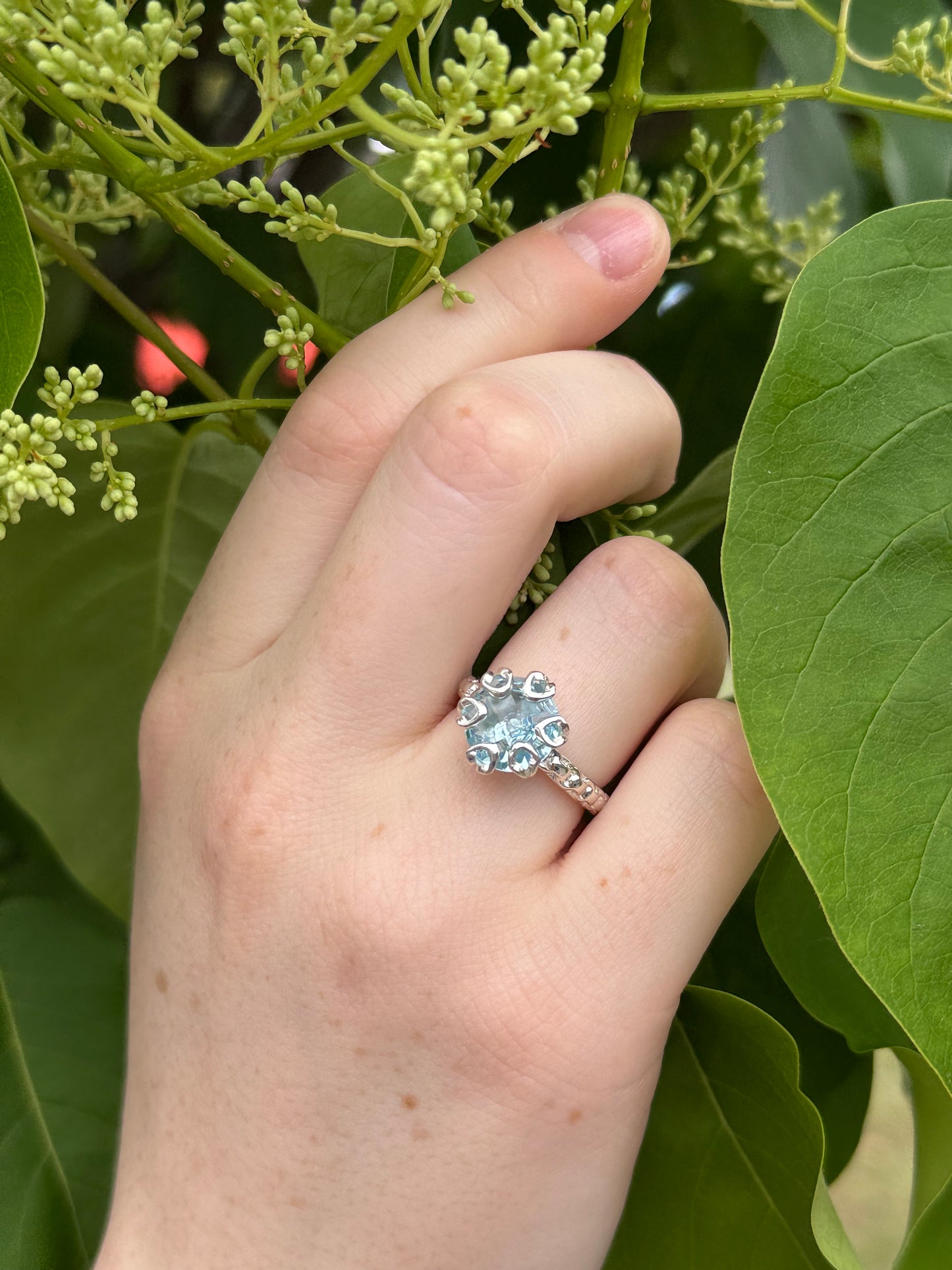 Hand wearing a ring with a green leafy background