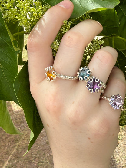 Hand wearing four silver rings with gemstones on green leaves