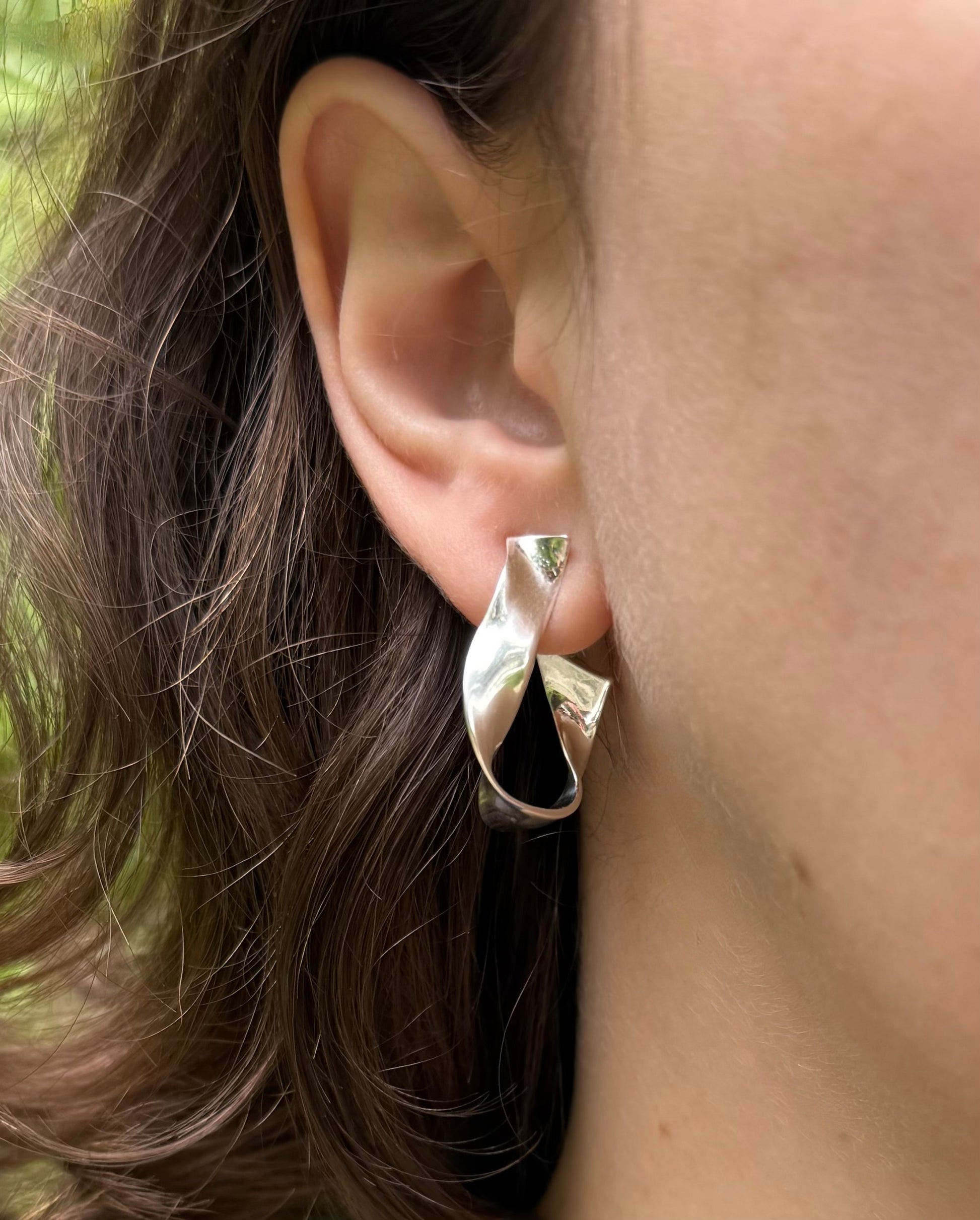 Silver earring worn by a person with brown hair.