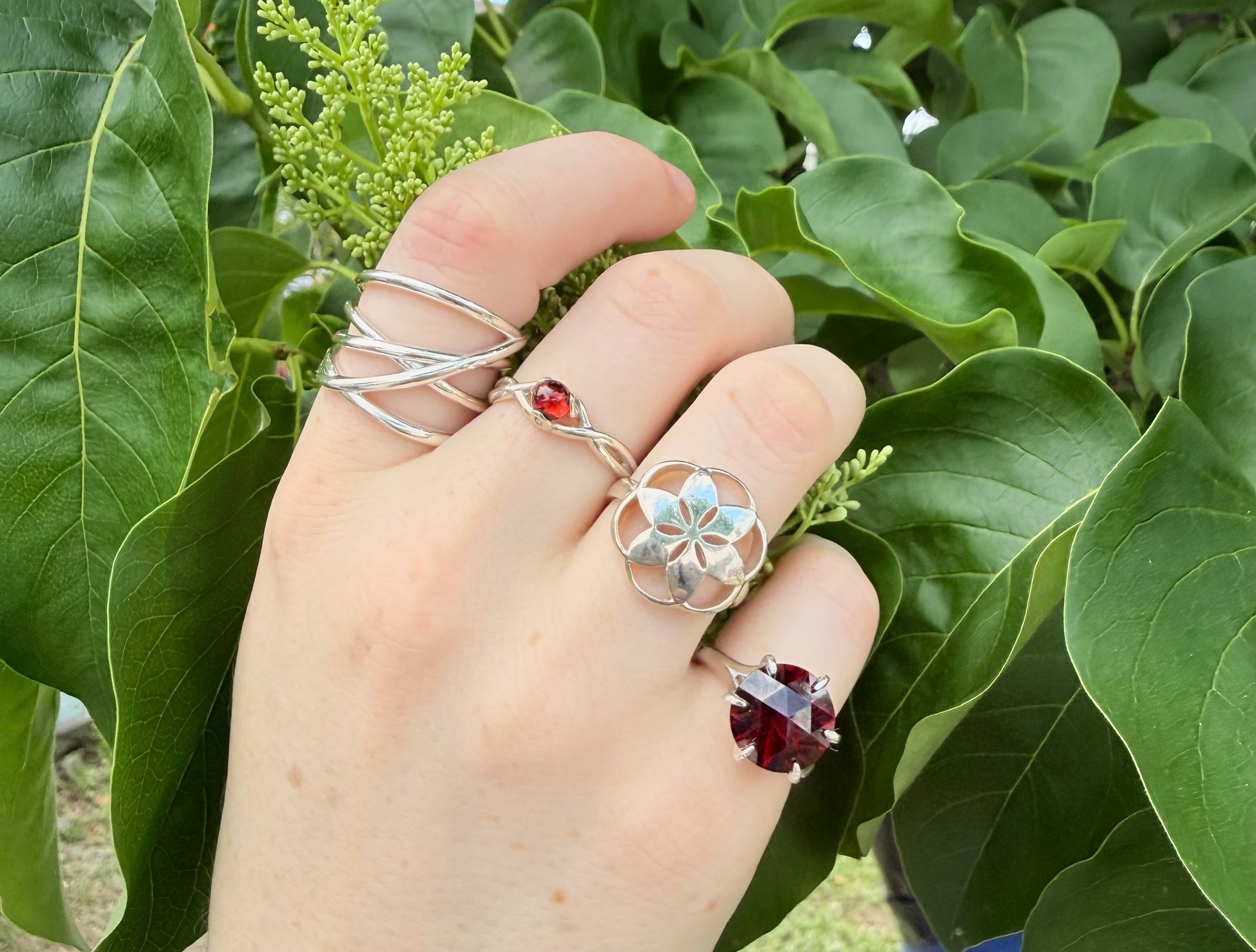 Hand wearing multiple rings with green leaves in the background