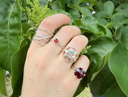 Hand wearing multiple rings with green leaves in the background