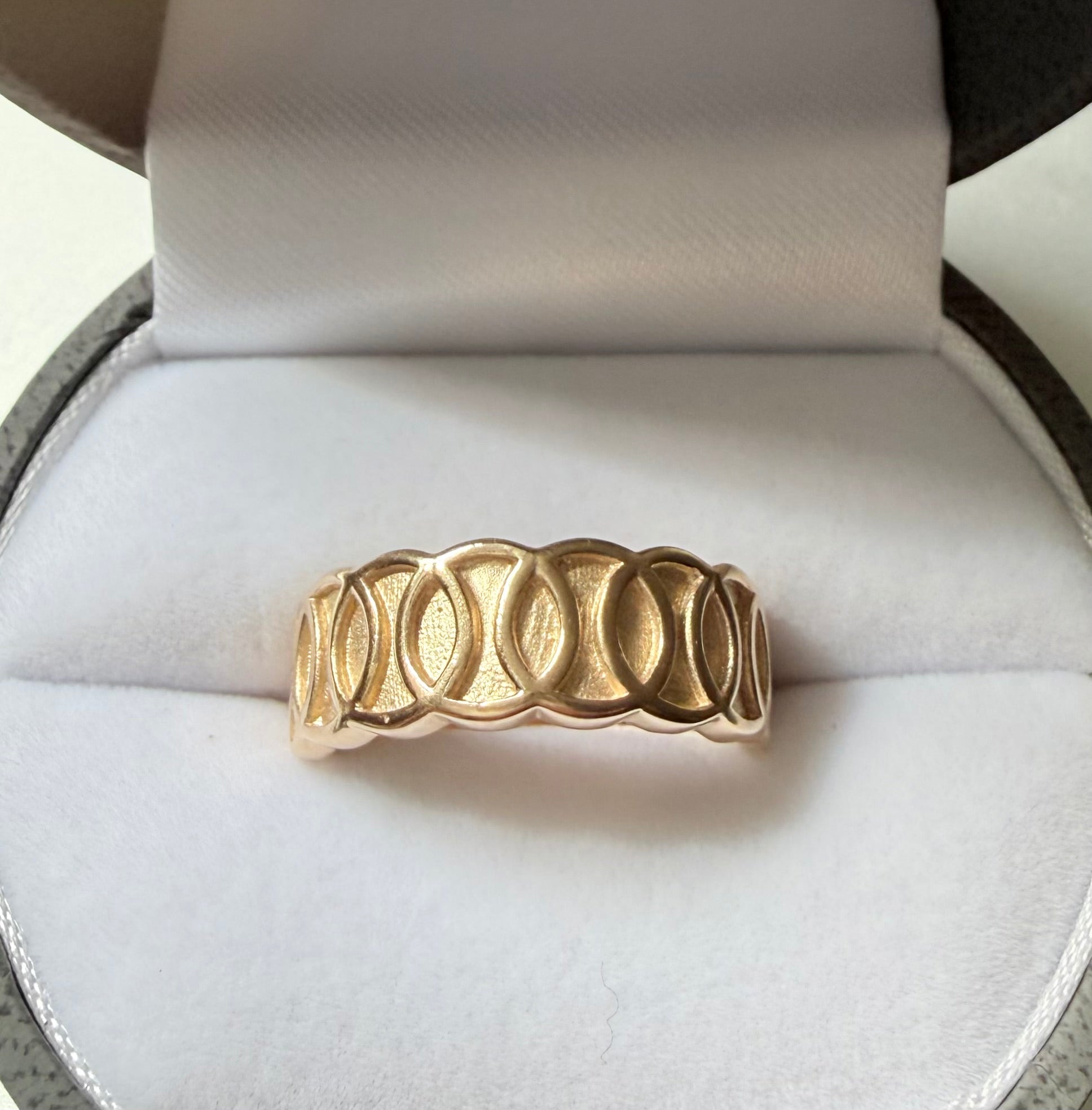 Gold ring with a unique design on a white cushion in an open jewelry box.