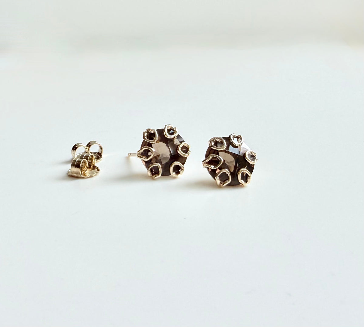 A pair of gold post earrings with a textured, organic, flower-like shape, displayed on a clean white surface.