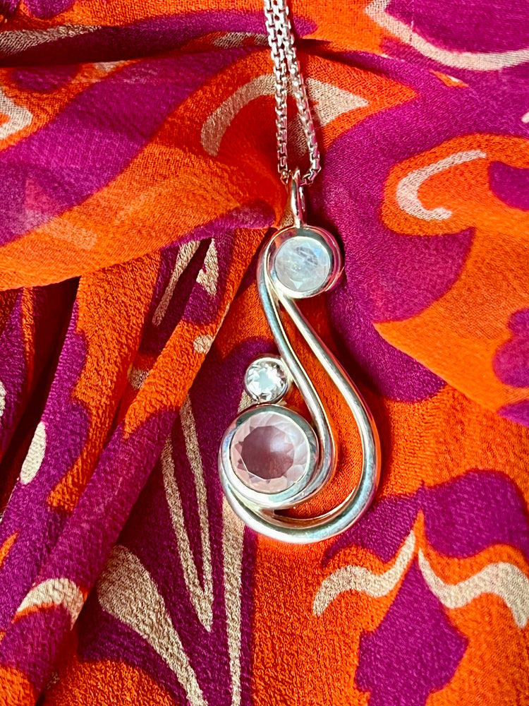 Aria Pendant by Hannah Daye & Com in Blush with Rose Quartz, White Topaz, Rainbow Moonstone on vibrant fabric of pink and orange
